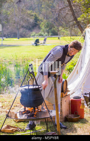 A man in period dress at a American Revolution reenactment cooking outdoors in a cast iron pot over a wood fire. Stock Photo