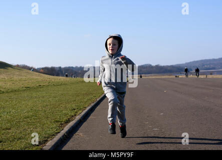 A six year old boy running with his hood up on a sunny winter day Stock Photo