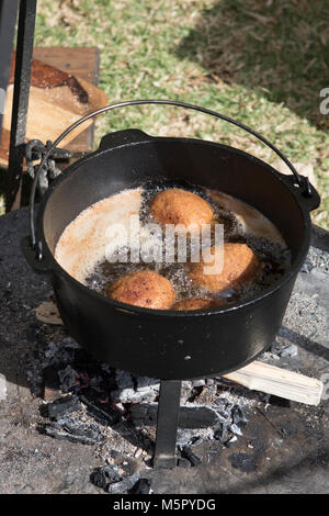 Deep frying golden brown scotch eggs outdoors over an open  wood fire in a heavy cast iron pot. Stock Photo