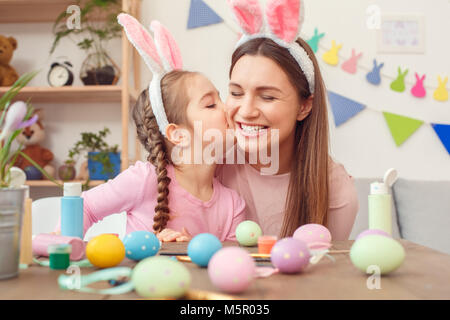 Mother and daughter together at home easter preparation in bunny ears sitting girl kissing mom Stock Photo