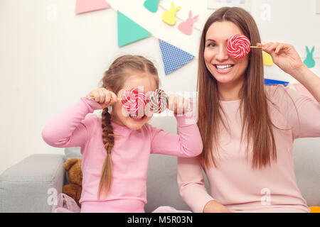 Mother and daughter weekend together at home covering eyes with lollipops Stock Photo