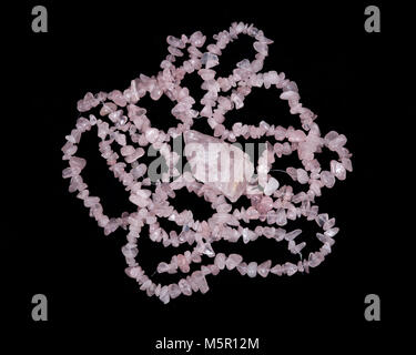 Raw rose quartz from Madagascar and polished rose quartz strings on black background Stock Photo
