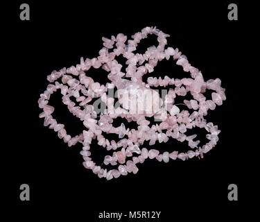 Raw rose quartz from Madagascar and polished rose quartz strings on black background Stock Photo