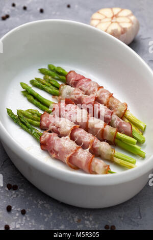 Baked asparagus with bacon in a white dish for baking on a gray background. view from above Stock Photo