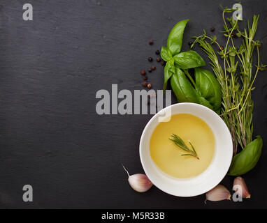 olive oil in a bowl, basil, thyme, rosemary, garlic on a black stone background. view from above Stock Photo