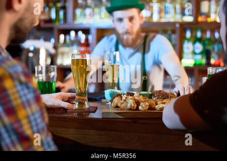 Traditional celebration of Saint Patricks Day: group of friends gathered together in pub, drinking fresh beer and chatting with each other Stock Photo