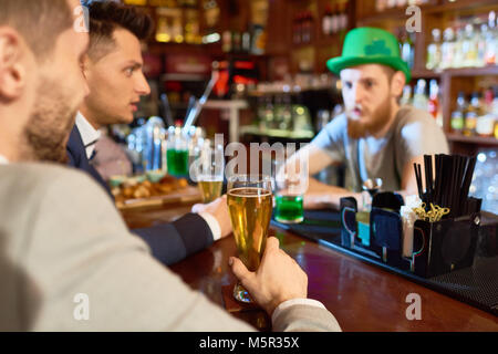 Handsome young businessmen wearing classical suits drinking beer and chatting with bearded barman while taking rest in pub after hard working day Stock Photo