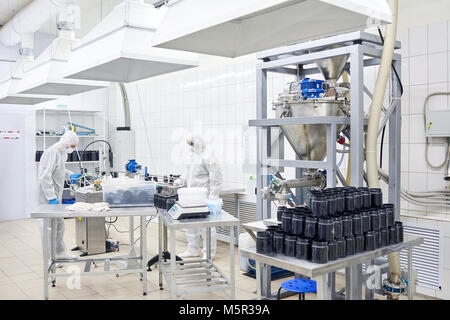 Team of highly professional factory workers wearing coveralls and safety masks taking inventory in warehouse of pharmaceutical factory Stock Photo