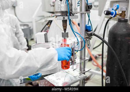 Unrecognizable factory worker wearing coverall and rubber gloves using bottle capping machine, close-up shot Stock Photo