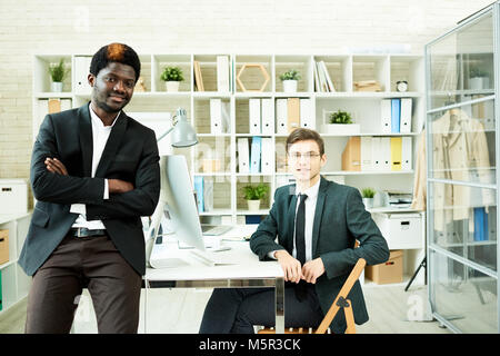 Multi-ethnic team of white collar workers wearing stylish suits posing for photography while gathered together in modern open plan office Stock Photo