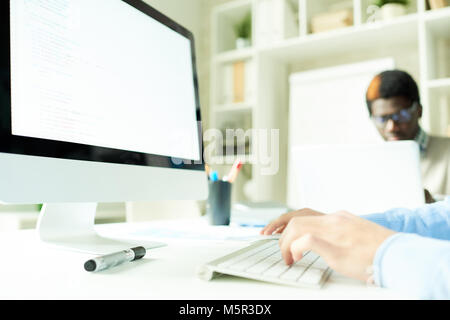 Close-up shot of unrecognizable manager sitting at desk and using computer with blank screen, interior of spacious open plan office on background Stock Photo