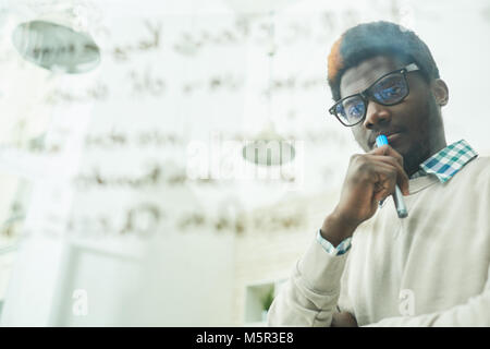 Waist-up portrait of pensive African American manager in eyeglasses standing at glass board and thinking over ambitious project, blurred background Stock Photo