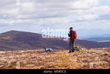 A hiker checking their position on a GPS map at the cairn marking Coomb Height in the English Lake District, UK. Stock Photo