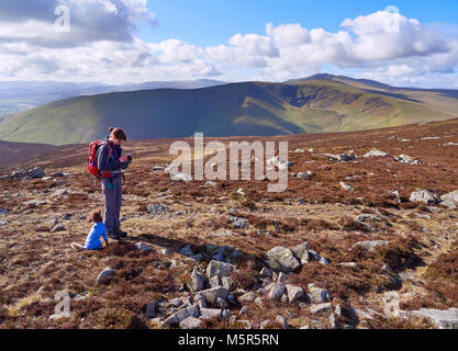 A hiker checking their position on a GPS map near the summit of Carrock Fell with views of Bowscale Fell and Blencathra in the distance in the English Stock Photo