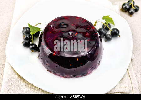 Jelly from black currant with berries in a plate on a napkin on the background of a stone table Stock Photo
