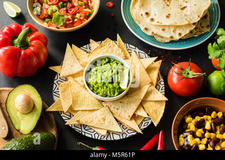 Mexican food Guacamole Nachos Tortilla chips salsa and beans on dark table. Food plate, Mexican cuisine Stock Photo