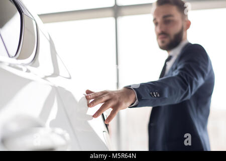 Portrait of handsome businessman gently touching smooth metal of white luxury car, focus on foreground, copy space Stock Photo
