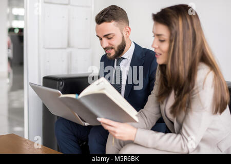 Portrait of two modern business people working in office, focus on beautiful businesswoman reading book Stock Photo