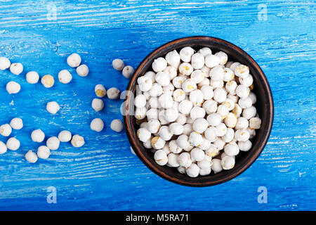 Chickpeas in a bowl on a blue wooden background, top view. Next to the plate is scattered chickpeas,  horizontal photo Stock Photo