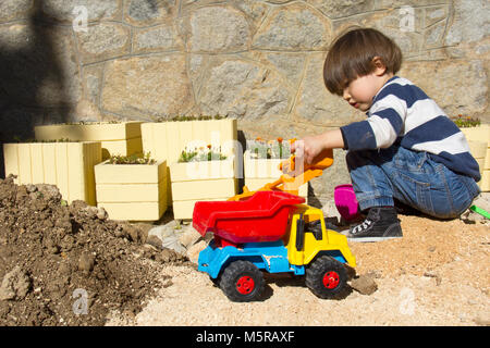 little three year old boy playing in the sand with a digger and dump truck. Stock Photo