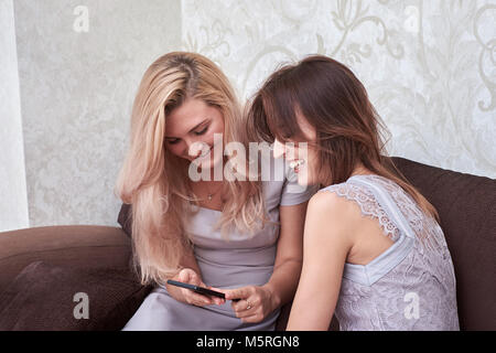 Girlfriends laugh at cell phone text, sitting on the sofa Stock Photo