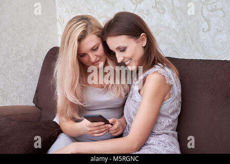 Girlfriends laugh at cell phone text, sitting on the sofa Stock Photo