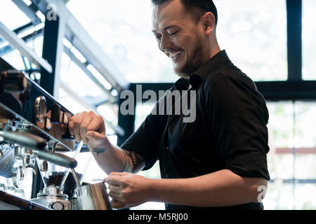 Young cheerful barista preparing coffee at an automatic machine  Stock Photo