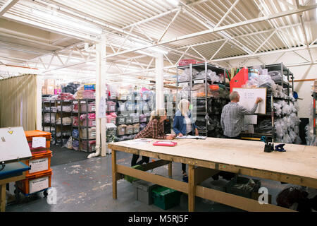 Senior employees are working together in an events warehouse making tablecloths. They are writing out measurements and discussing them. Stock Photo