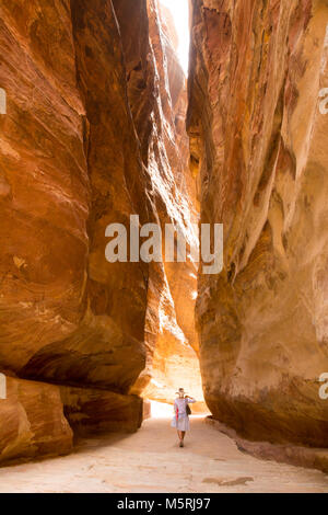 PETRA, JORDAN - APRIL 25, 2016: A narrow passage between steep rock formations in the siq at Petra the ancient City Al Khazneh in Jordan lit by the su Stock Photo