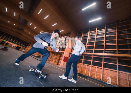 Two young skaters are performing tricks with their skateboards in an indoor skate hall. Stock Photo