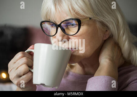 Portrait of pensive senior lady in glasses having cup of tea Stock Photo