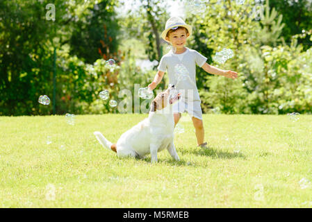 Happy kid and pet dog playing with soap bubbles at backyard lawn Stock Photo
