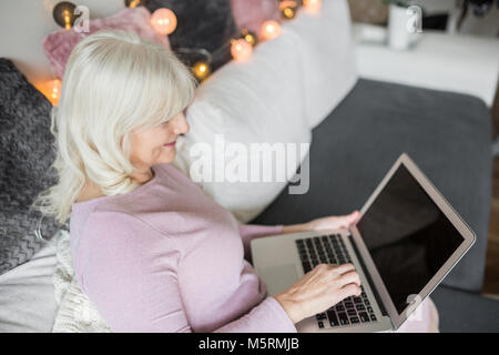 Portrait of glad senior lady relaxing on couch using notebook Stock Photo