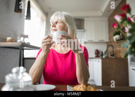 Portrait of glad senior lady sitting at kitchen table having cup of coffee Stock Photo