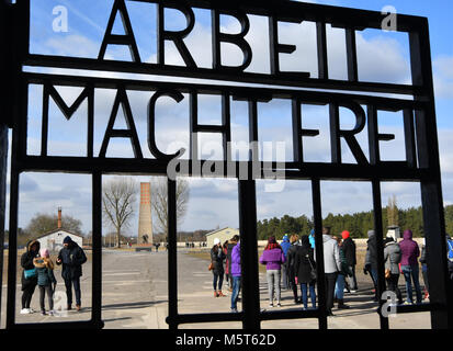 25 February 2018, Germany, Oranienburg: Visitors walk past the cast iron entrance gate with the writing 'Arbeit macht frei' (lit. work sets you free) at the memorial site of former Sachsenhausen concentration camp. A new depot was opened on the site of the industrial area of the former concentration camp which exhibits 35,000 original objects from the camp and the belongings of survivors. Photo: Bernd Settnik/dpa-Zentralbild/dpa Stock Photo