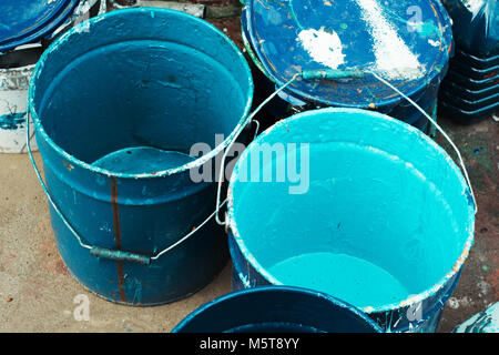 Paint dirty bucket with blue color on asphalt with paintbrush.Old paint in messy, rusty cans ready for recycling. Close up. Stock Photo