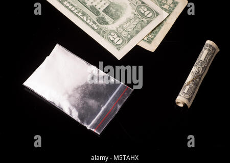 cocaine, Herion or other illegal drugs that are sniffed by means of a tube or injected with a syringe and money, isolated on black glossy background Stock Photo