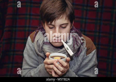 Sick teenager with a thermometer at home. Concept of health. Stock Photo