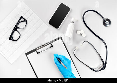 Doctor s table, tools, medical instruments, stethoscope, work in hospital on white background flat lay. The doctor's hand in a blue glove records the  Stock Photo