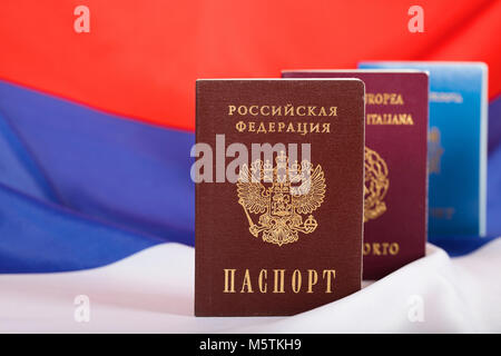 Russian pass in front of Moldovan and Italian ones. Russian flag in the background.Translation on the pass- Russian Federation. Passport. EU. Italian  Stock Photo