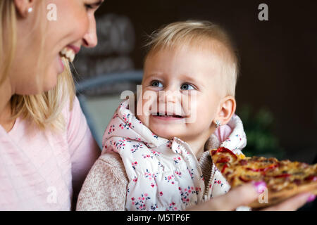 Little girl eats a large slice of pizza from her mother's hands. Children's pizza. Stock Photo