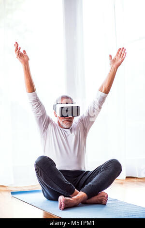 Senior man with VR goggles doing exercise at home. Stock Photo