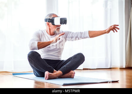 Senior man with VR goggles doing exercise at home. Stock Photo