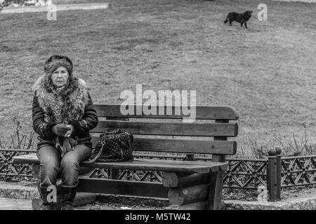 Lonely elderly woman on a bench in the park, black and white reportage photograph Stock Photo