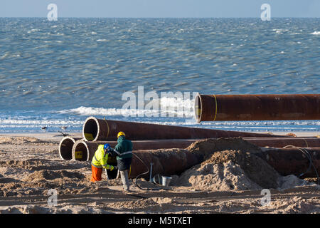 Dredging workers connecting pipes of pipeline during sand replenishment / beach nourishment works along the Belgian coast at Ostend, Belgium Stock Photo