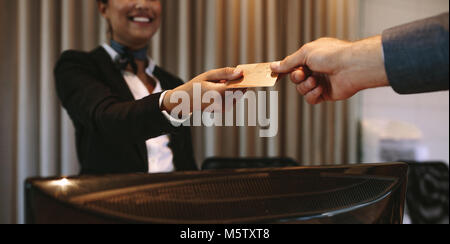 Close up of businessman paying with credit card at reception desk in hotel. Business man giving credit card to hotel receptionist for payment of his r Stock Photo