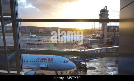 ZURICH, SWITZERLAND - MAR 31st, 2015: Airport view through window of waiting area - planes of SWISS airline in a row at the gates during sunshine Stock Photo