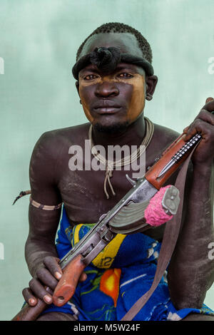 A Portrait Of A Young Man From The Mursi Tribe Holding A Gun, Mursi Village, Omo Valley, Ethiopia Stock Photo