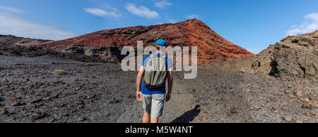 A man with a backpack trekking in volcanic landscape of Timanfaya National Park on Lanzarote, the Canary Islands, Spain Stock Photo