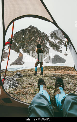 Travel lifestyle camping couple view from tent entrance woman walking in mountains man feet relaxing inside adventure vacations outdoor Stock Photo